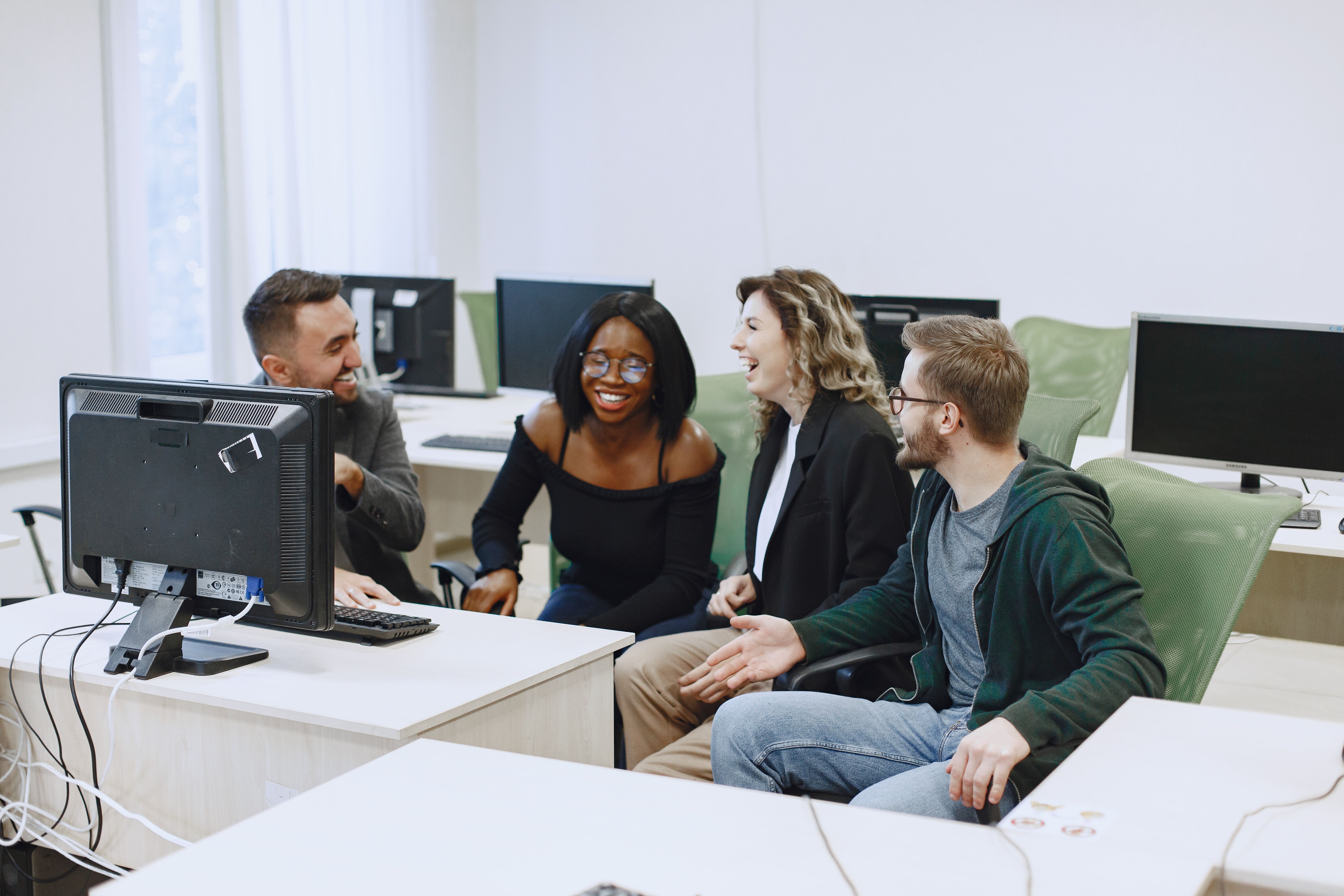 A group of people laughing together around a computer at the Tech-Futures center.
